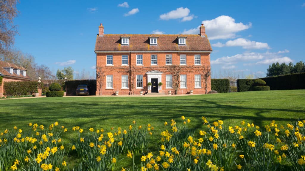 Elegant English Country Manor mansion house Grade 2 listed Victorian period property in red brick. Front view with large garden, green lawn and daffodils