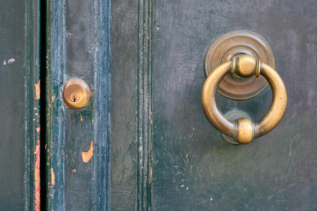 Close-up of an old, weathered green wooden door featuring a brass knocker and keyhole, highlighting its age and history