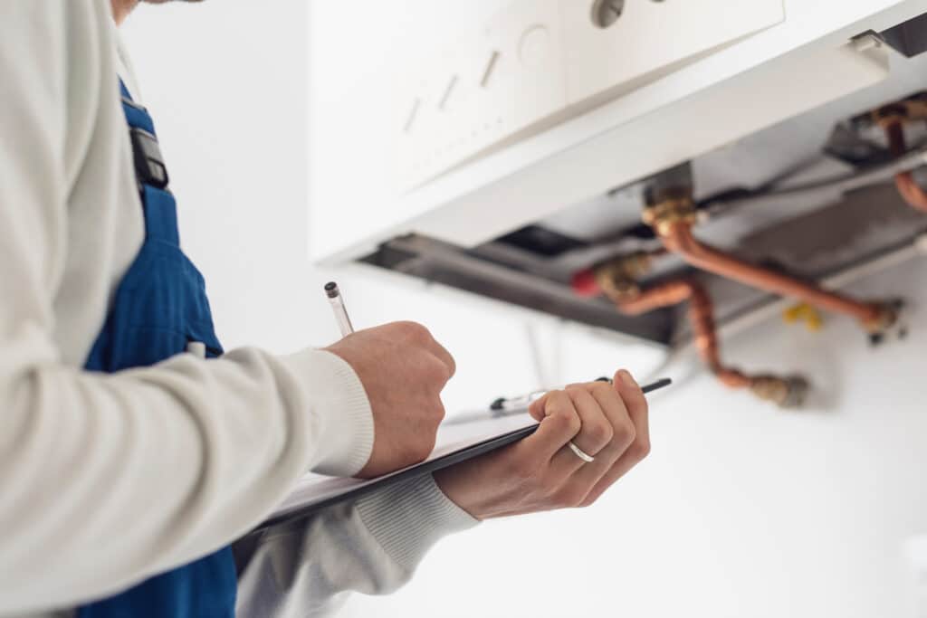 Professional plumber checking a boiler at home and writing on a clipboard