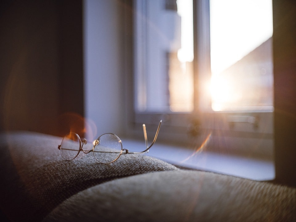 Pair of glasses next to a window with the sun rising from the background